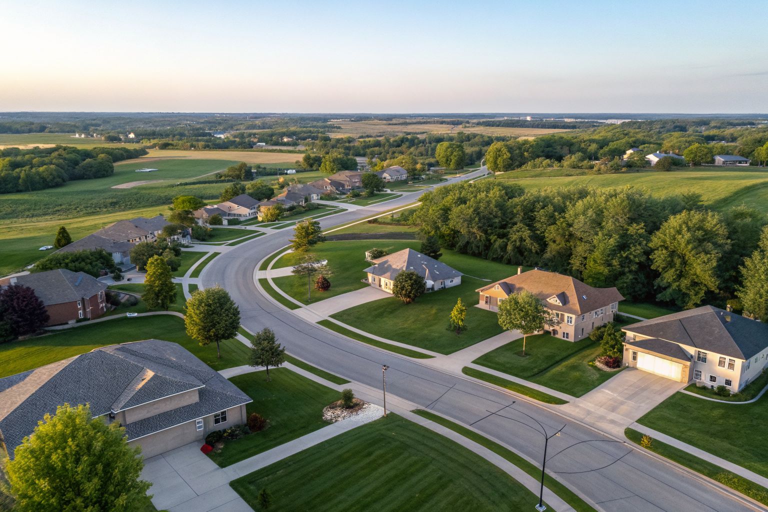 Aerial view of a suburb with curving streets, shingle roofs and green lawns on gently rolling land